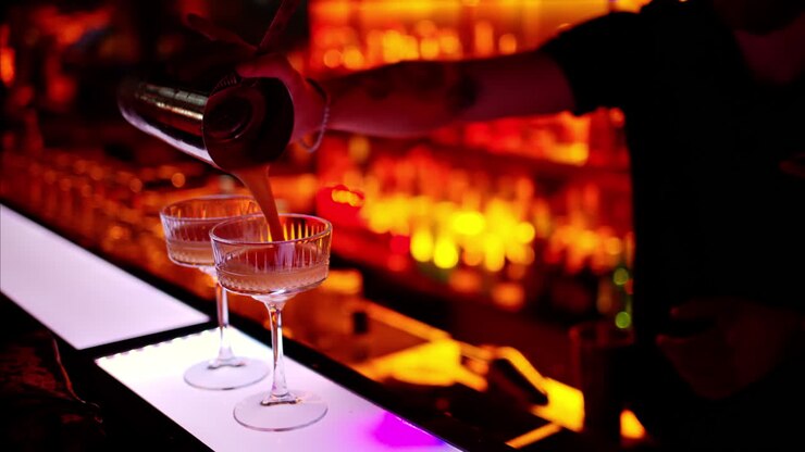Barman che prepara un cocktail con spumante bianco al bar di notte con luci al neon rosse, slow motion