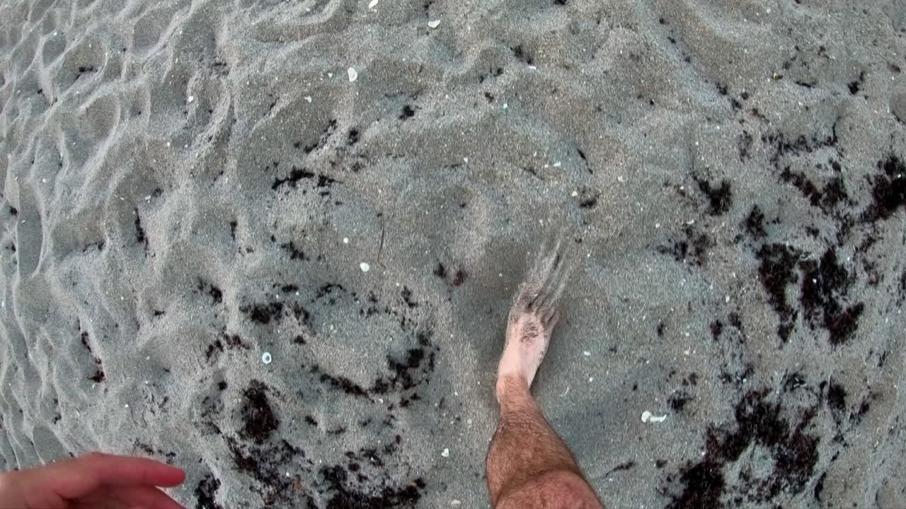 Piedi di uomo che camminano su una spiaggia sabbiosa in una giornata nuvolosa