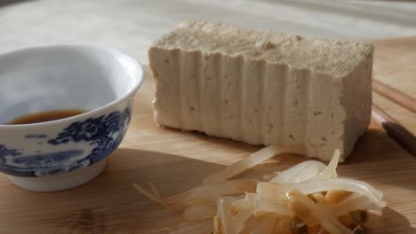 tofu block, soy sauce in porcelain bowl and bean sprouts on wooden surface, sunny light