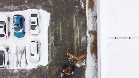 snowplow clearing parking lot during spring storm in longueuil, aerial view