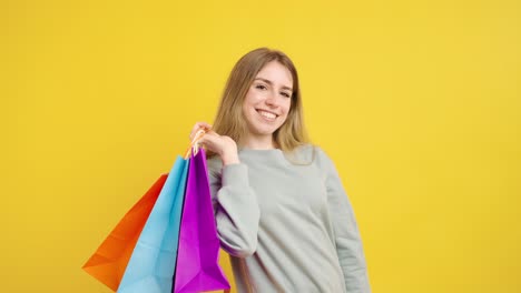 young woman showing shopping bags on yellow background