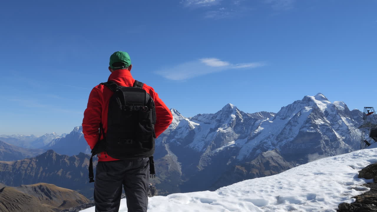 Man wearing a backpack looking at the Eiger, Monch, and Jungfrau mountains in Switzerland