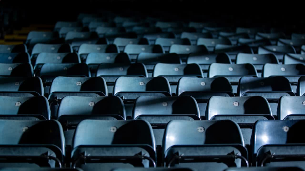 Mostrando sedili pieghevoli che riflettono punti freddi dopo uno spostamento della telecamera per un'arena vuota, con placche numeriche.