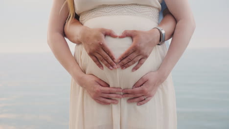 a young couple shows a heart on the belly of a pregnant woman