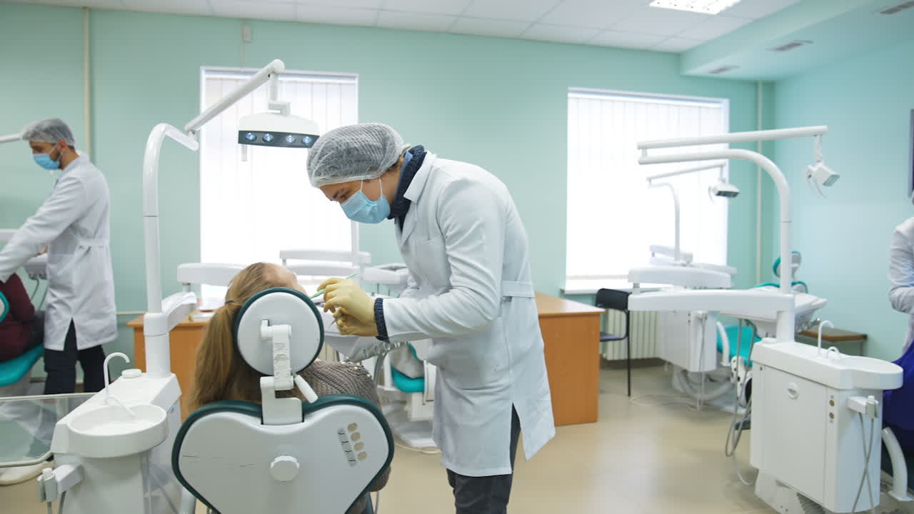 Big light classroom with lots of dentistry chairs occupied by patients and students beside them. Future dentists practicing on people.