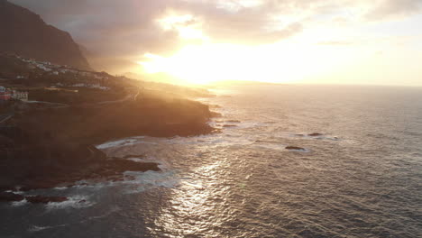 flying above the coastline with beautiful sunset light at benijo beach in tenerife, canary islands. big wave is crashing on rocks and spraying.