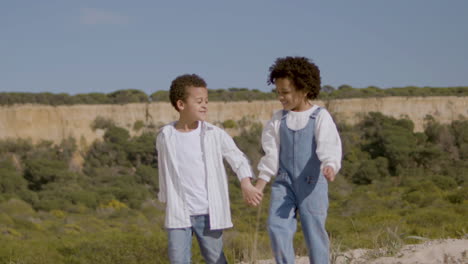 Two-Happy-American-Siblings-Walking-In-Natural-Park-And-Holding-Hands-On-A-Warm-Sunny-Day