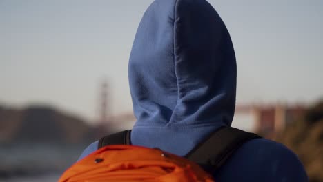 cerca de un tipo con capucha azul caminando en la playa de los panaderos en san francisco con el puente golden gate en el fondo