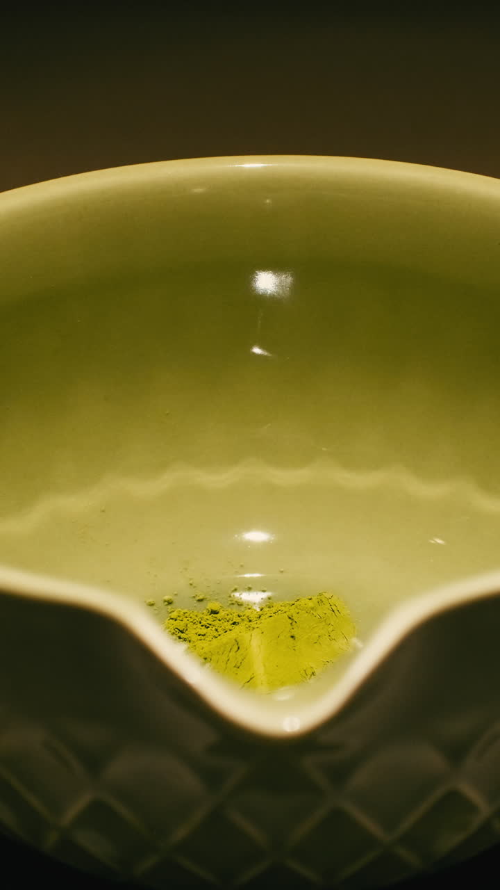 Macro vertical footage of green matcha tea powder being prepared with hot water in a ceramic bowl. Perfect for social media content about wellness and healthy lifestyle