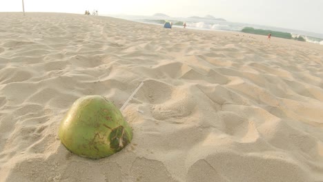 rotating around solitary empty coconut with a transparent plastic straw sticking out left behind on the beach