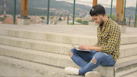 handsome man siting on stairs using laptop outdoors