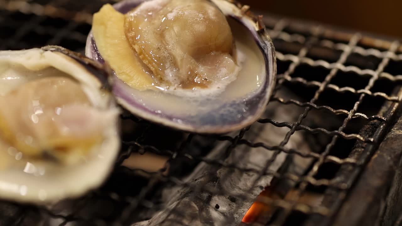 Detailed view of scallops cooking in shells over a hot grill, showcasing texture and heat.