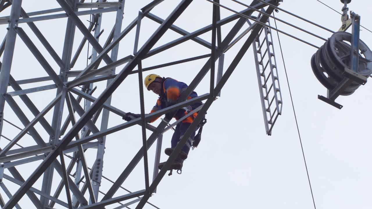 Man skillfully works high up on pylon and power lines, hoisting a ladder up