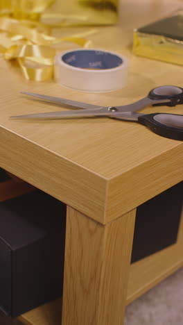 vertical video of gift or present being wrapped on table at home with scissors sticky tape and ribbon