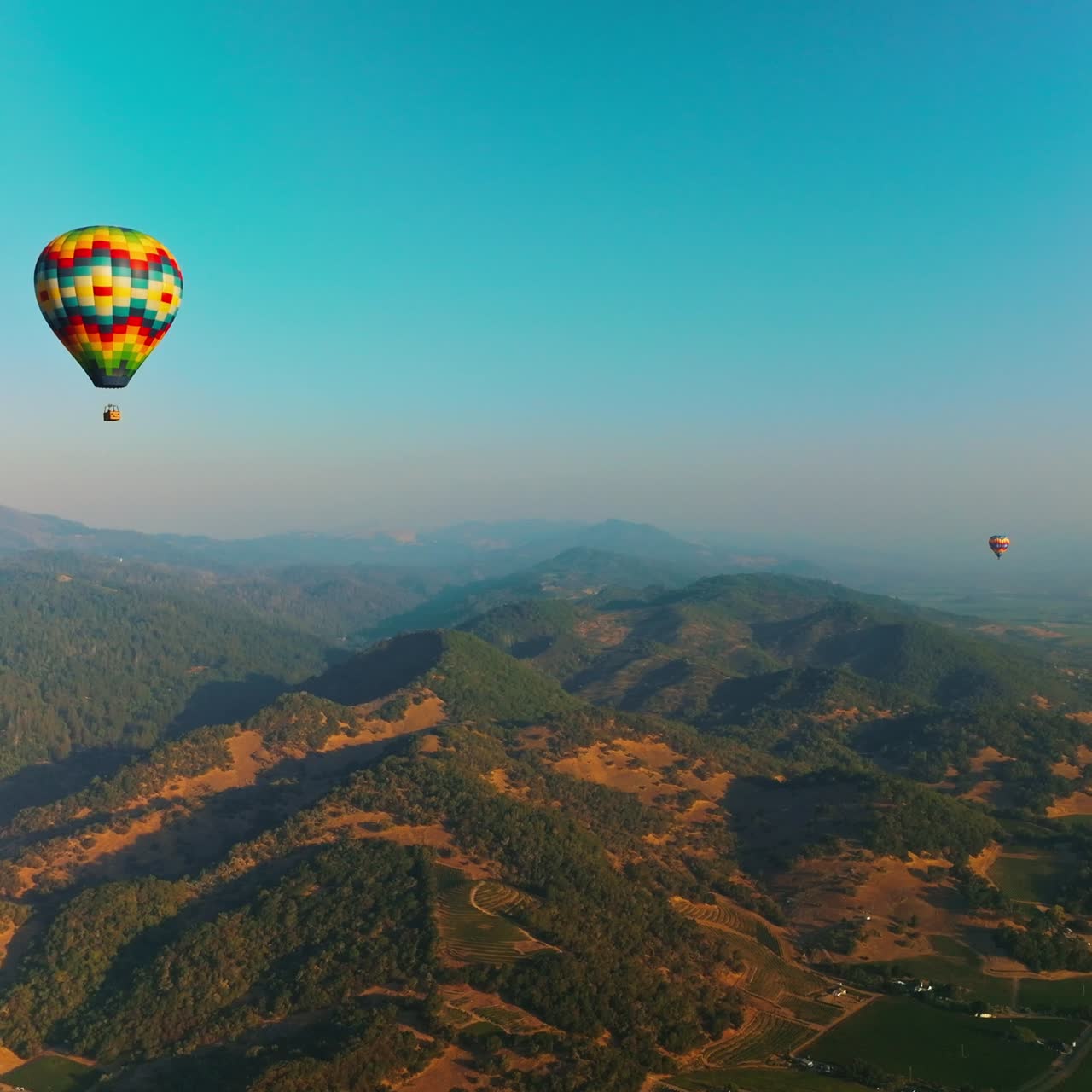 Colorful hot air balloons soaring over the green hills. Picturesque panorama of Napa valley in California, USA. Aerial view
