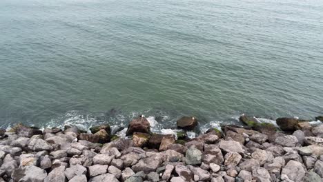 aerial view above splashing ocean tide breaking on rocky coastal shoreline slow pan left
