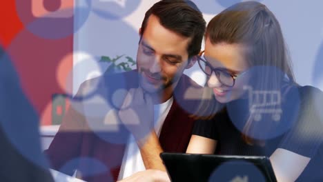 Animation of multiple digital icons against diverse man and woman discussing at office