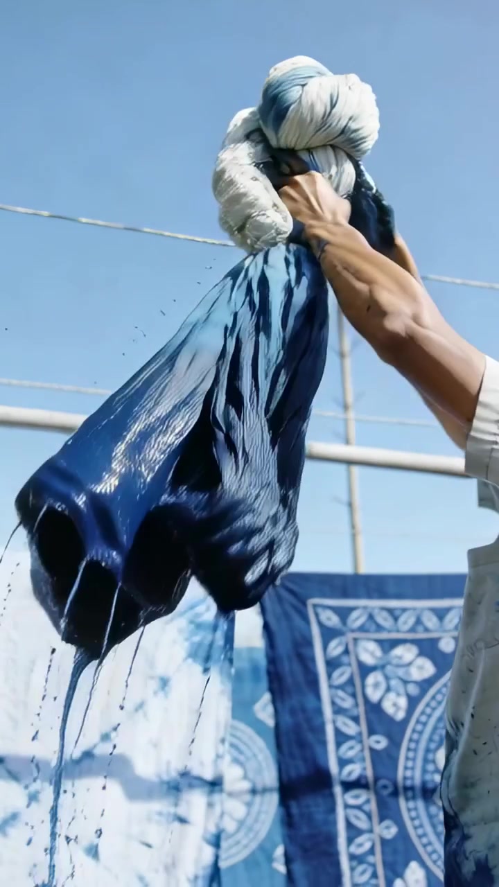 Vertical video: Lifting wet indigo cloth gloved dyer wringing to hang on roof line, copy space