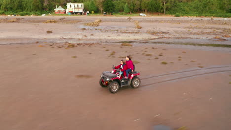 aerial shot following people riding a quad bike around a sandy coastal beach, bright sunny daylight