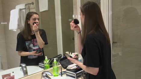 teenage girl applying makeup in bathroom