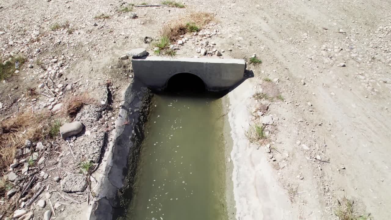 Zoom avanti con drone che si avvicina a uno stretto canale di irrigazione con acqua corrente che supporta l'irrigazione delle colture nei campi agricoli di Barahona, Repubblica Dominicana