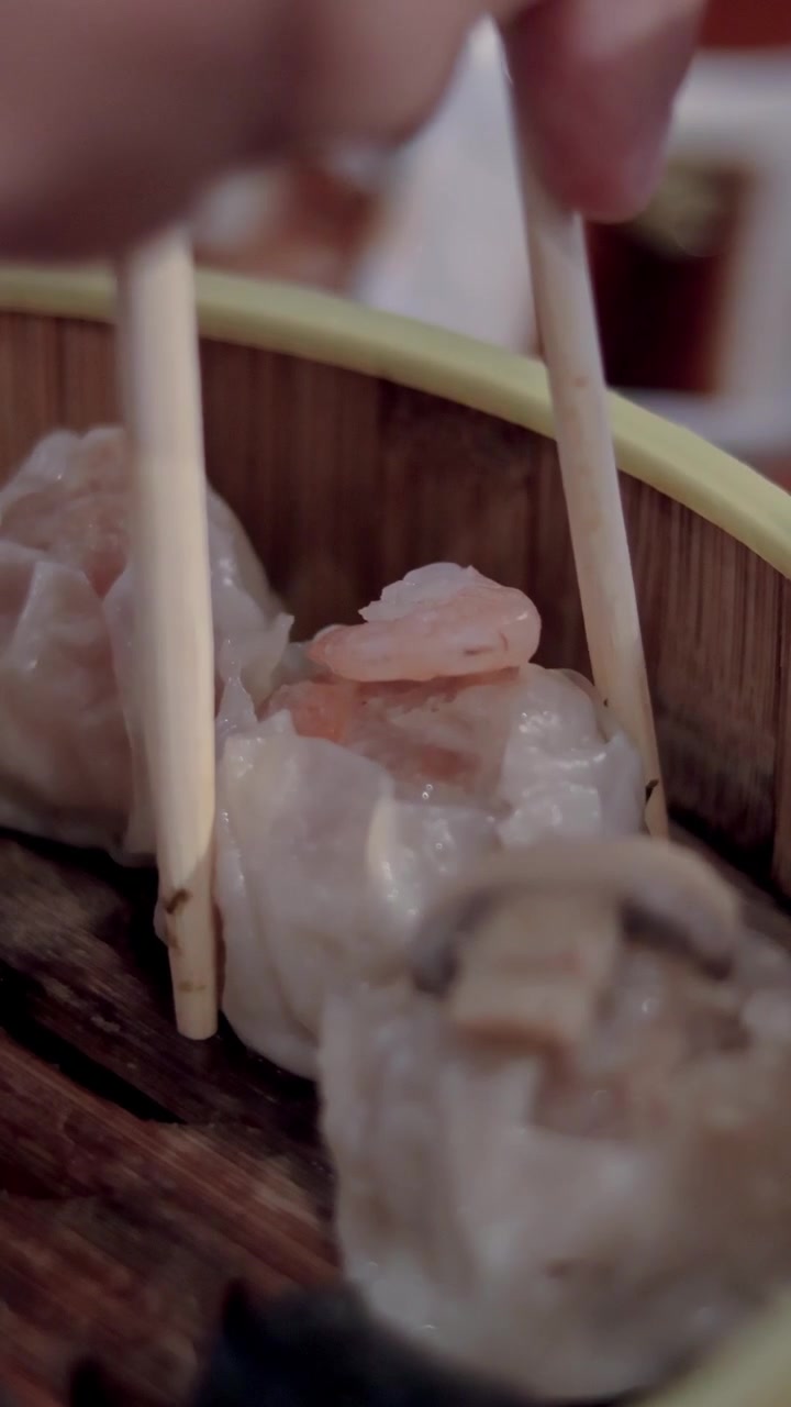 Detail shot close-up to chopsticks picking up shrimp siomai or siu mai dumpling from a bamboo steamer during a dim sum meal