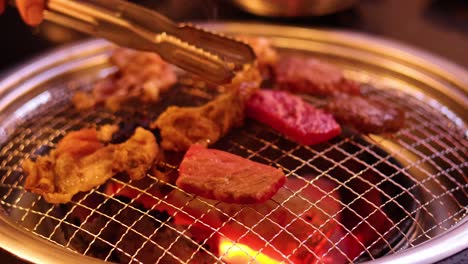 tongs flipping meat on a barbecue grill