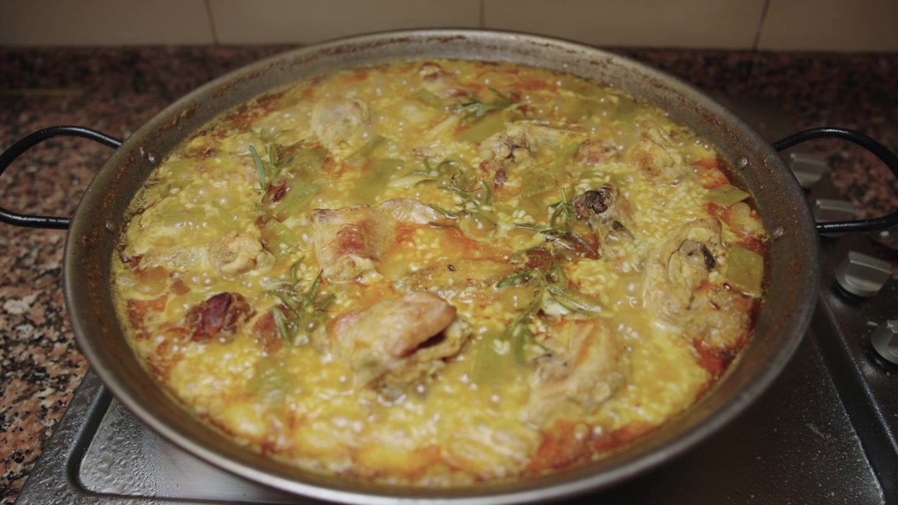 Primo piano di una paella valenciana spagnola tradizionale con pollo e fagiolini che bolle e sobbolle in una padella su un fornello a gas, al rallentatore.