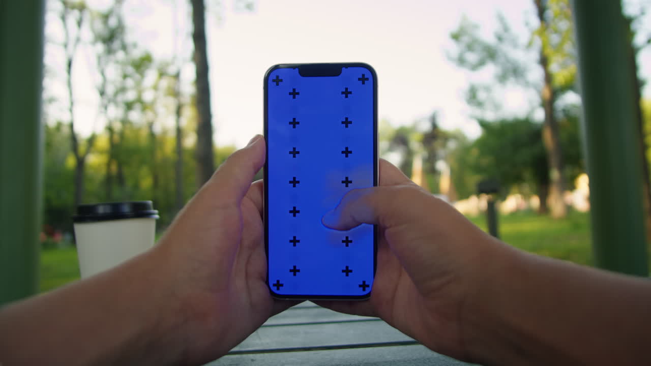 Young woman holding and swiping phone chroma key screen in the park in front of trees close-up. Girl with green screen on smart phone. Nature