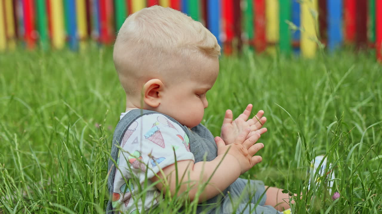 A 10-month-old baby boy is playing while sitting on the grass. A child in nature