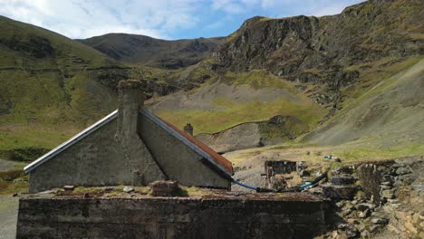 Altes-Haus-Mit-Rostigem-Blechdach-In-Bergkulisse-Bei-Force-Crag-Mine-Coledale-Beck-Im-Englischen-Lake-District