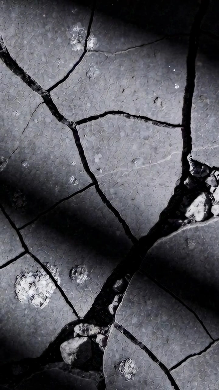 Video verticale: Ombra che si sposta mostrando un primo piano di un marciapiede crepato da un lento cambiamento di luce, con pietre