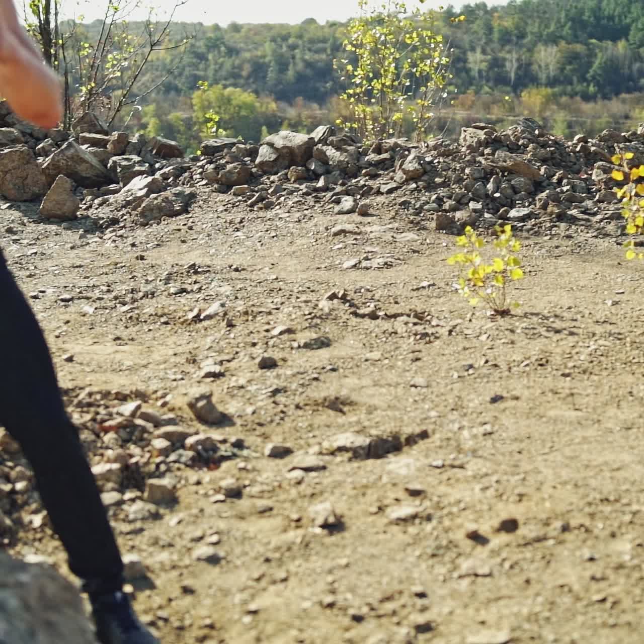Strong athlete training his body by throwing stones. Muscular shirtless guy doing his hard workout with rocks among nature in summer. Slow motion.