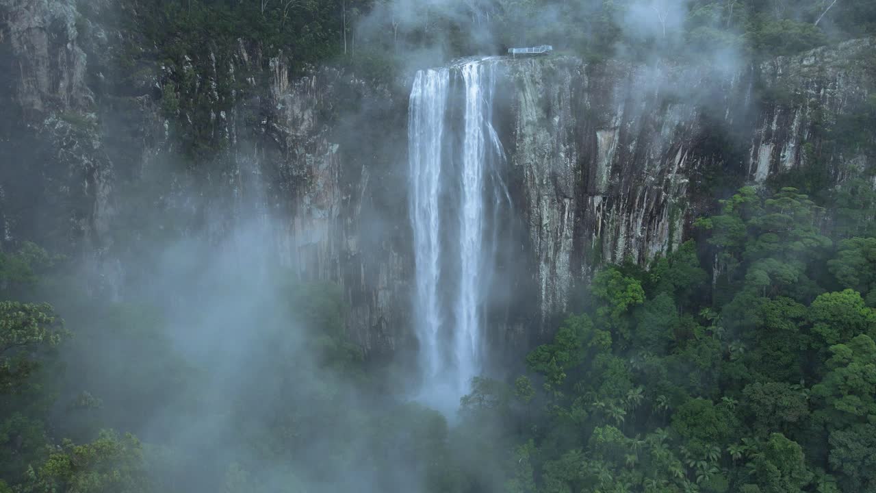 vista cinematográfica mirando a través de la creciente niebla que revela una majestuosa cascada que se derrama sobre una exuberante montaña cubierta de selva tropical