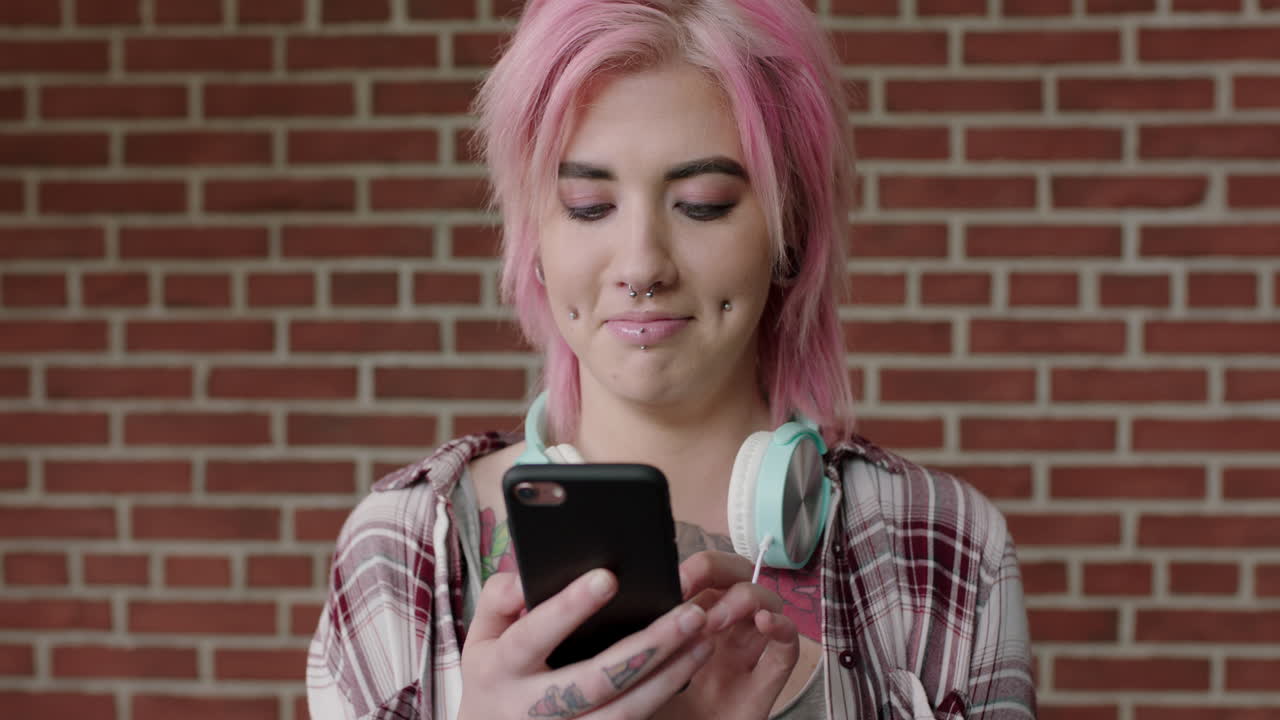 ritratto di una donna punk alternativa con i capelli rosa che manda sms navigando sui social media usando lo smartphone
