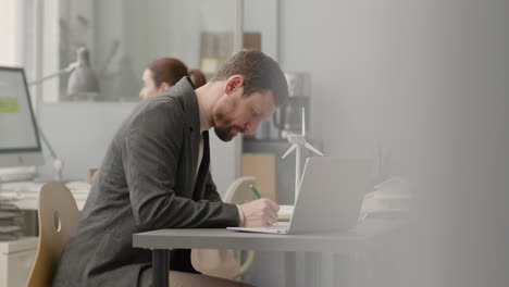 nahaufnahme eines nicht erkennbaren mannes, der auf einer blaupause schreibt, die am schreibtisch im büro sitzt