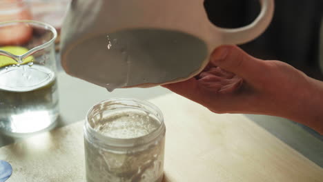 a person pours a ceramic glaze from a cup into a container - close up