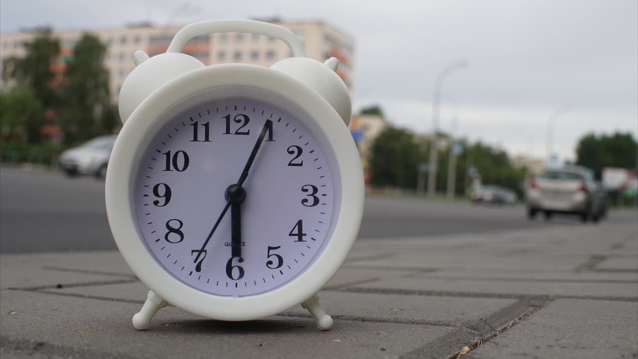 Clock in the form of an alarm clock in a fast-moving timelapse, the hands move, against the background of fast-passing car traffic in a city or metropolis. The concept of fast-moving time.