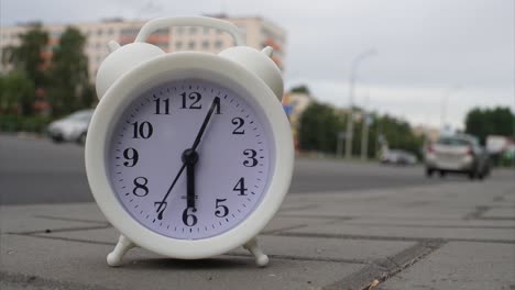 reloj en forma de despertador en un lapso de tiempo de movimiento rápido, las manillas se mueven, contra el fondo del tráfico de automóviles de paso rápido en una ciudad o metrópolis. el concepto de tiempo de paso rápido.