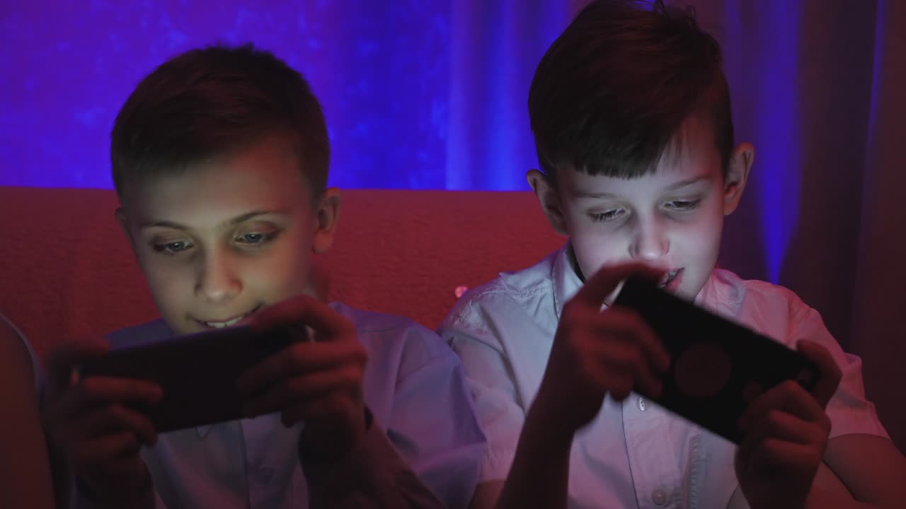 두 명의 귀여운 소년이 방에서 스마트 폰으로 비디오 게임을 하고 있습니다.