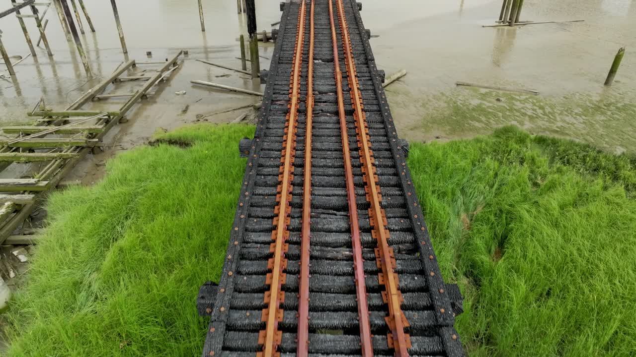 Blackened Railway Tracks Stretch Across the Muddy Riverbed in Richmond, British Columbia, Canada - Aerial Pullback Shot