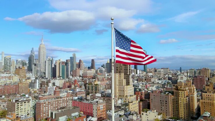 Slow Motion Aerial orbiting around USA flag waiving with blue sky and Manhattan in the background