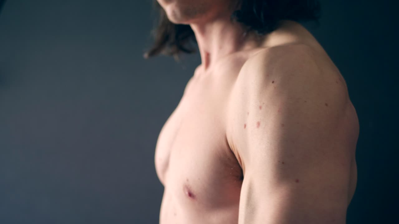 un fuerte fisicoculturista blanco sin camisa flexionando los músculos de su brazo en el gimnasio después de un duro entrenamiento de fitness