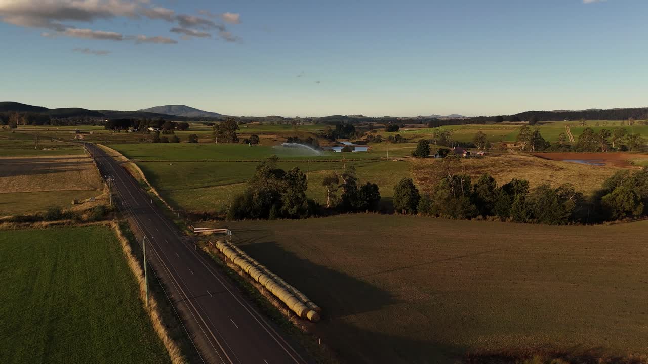 Plano aberto 4K60 de uma paisagem idílica da Tasmânia com estrada rural e campos verdes, montanhas ao fundo.