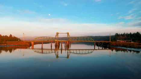 Drone-Volando-Sobre-El-Puente-Bullards-Con-Reflejo-Especular-En-El-Río-Coquille-Durante-La-Puesta-De-Sol-Cerca-Del-Refugio-Nacional-De-Vida-Silvestre-Bandon-Marsh-En-Oregon,-Estados-Unidos