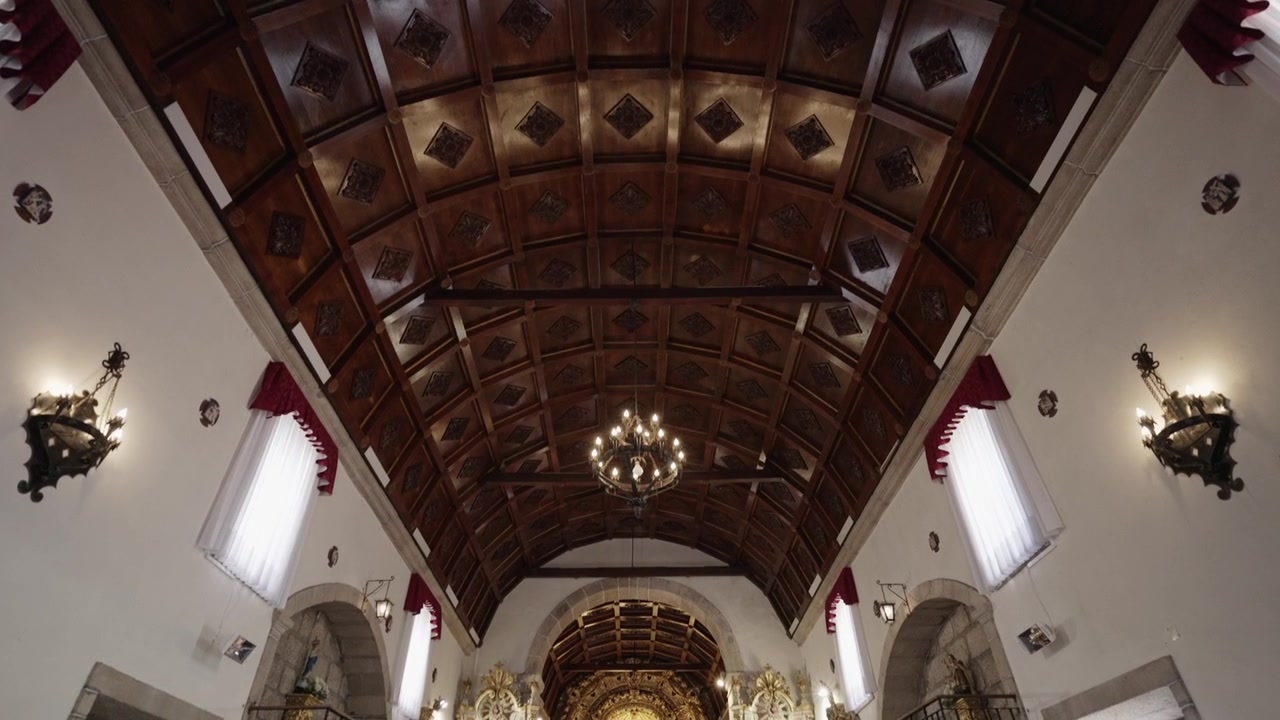Church ceiling with wooden beams, chandeliers, and ornate details in soft, warm lighting