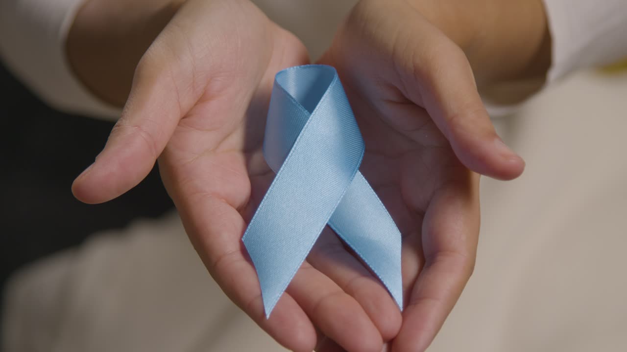 Close Up Of Person Holding Blue Ribbon Symbolizing Awareness Of Men's Health And Cancer