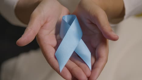 primer plano de una persona que sostiene una cinta azul que simboliza la conciencia de la salud de los hombres y el cáncer