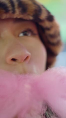 close-up of a person with a leopard print hat and eyeliner, enjoying cotton candy
