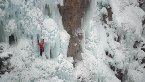 ice climber with axe climbing on frozen waterfall in cold snowy winter landscape wide view